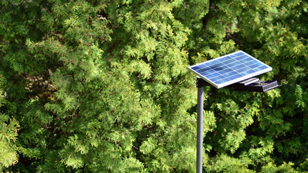 Lighting pole with photovoltaic panel and LED lamp lights with green background on in garden....