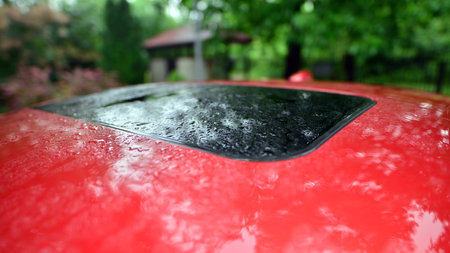 Raindrops falling on the roof of a red car.の写真素材