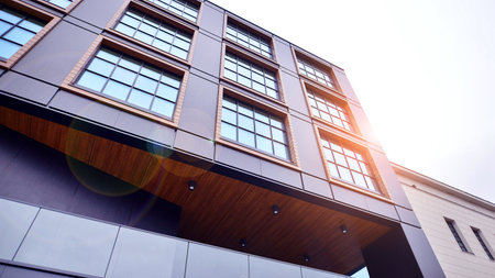 A view at a straight facade of a modern building with a dark gray facade. Dark gray metallic panel...