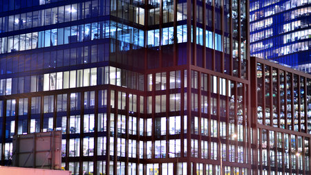 Office building in the evening with lightened workspaces. Modern, glazed skyscraper in financial district. Late hours in the office.の写真素材