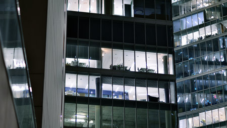Office building in the evening with lightened workspaces. Modern, glazed skyscraper in financial district. Late hours in the office.の写真素材