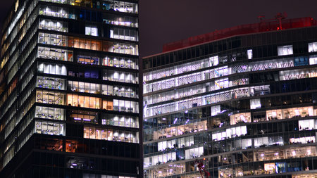 Office building in the evening with lightened workspaces. Modern, glazed skyscraper in financial district. Late hours in the office.の写真素材