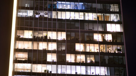 Office building in the evening with lightened workspaces. Modern, glazed skyscraper in financial district. Late hours in the office.の写真素材