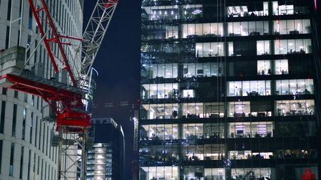 Office building in the evening with lightened workspaces. Modern, glazed skyscraper in financial district. Late hours in the office.の写真素材