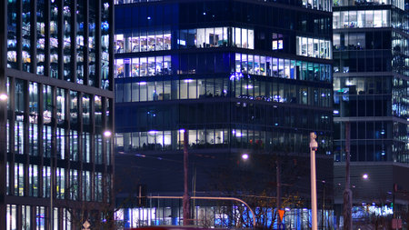 Office building in the evening with lightened workspaces. Modern, glazed skyscraper in financial district. Late hours in the office.の写真素材
