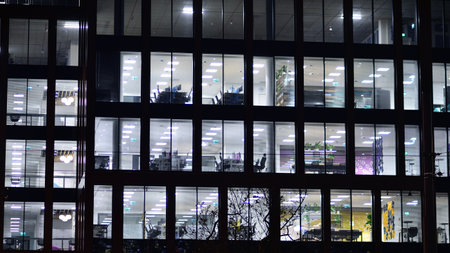 Office building in the evening with lightened workspaces. Modern, glazed skyscraper in financial district. Late hours in the office.の写真素材