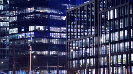 Office building in the evening with lightened workspaces. Modern, glazed skyscraper in financial district. Late hours in the office.の写真素材