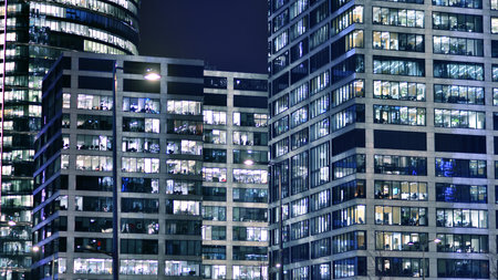 Office building in the evening with lightened workspaces. Modern, glazed skyscraper in financial district. Late hours in the office.の写真素材