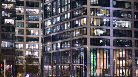 Office building in the evening with lightened workspaces. Modern, glazed skyscraper in financial district. Late hours in the office.の写真素材