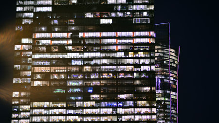 Office building in the evening with lightened workspaces. Modern, glazed skyscraper in financial district. Late hours in the office.の写真素材