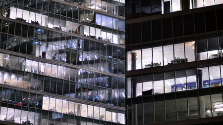 Office building in the evening with lightened workspaces. Modern, glazed skyscraper in financial district. Late hours in the office.の写真素材