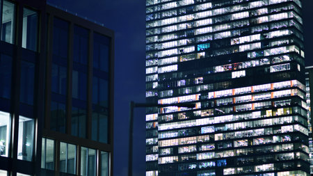 Office building in the evening with lightened workspaces. Modern, glazed skyscraper in financial district. Late hours in the office.の写真素材
