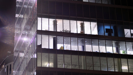 Office building in the evening with lightened workspaces. Modern, glazed skyscraper in financial district. Late hours in the office.の写真素材