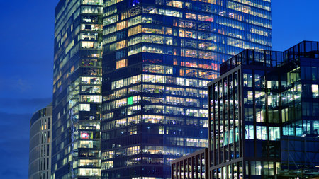 Office building in the evening with lightened workspaces. Modern, glazed skyscraper in financial district. Late hours in the office.の写真素材