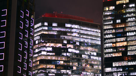 Office building in the evening with lightened workspaces. Modern, glazed skyscraper in financial district. Late hours in the office.の写真素材