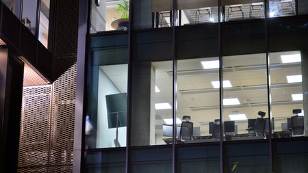 Office building in the evening with lightened workspaces. Modern, glazed skyscraper in financial district. Late hours in the office.の写真素材