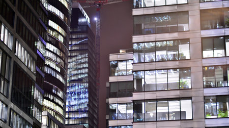 Office building in the evening with lightened workspaces. Modern, glazed skyscraper in financial district. Late hours in the office.の写真素材