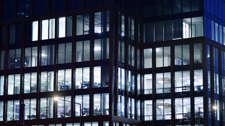 Office building in the evening with lightened workspaces. Modern, glazed skyscraper in financial district. Late hours in the office.の写真素材