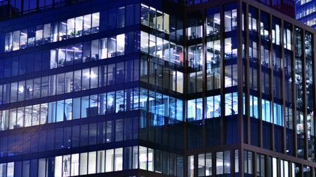 Office building in the evening with lightened workspaces. Modern, glazed skyscraper in financial district. Late hours in the office.の写真素材