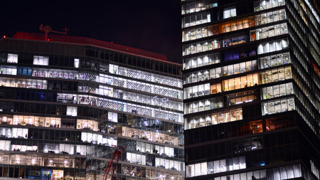 Office building in the evening with lightened workspaces. Modern, glazed skyscraper in financial district. Late hours in the office.の写真素材