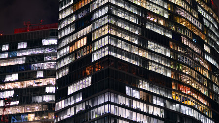 Office building in the evening with lightened workspaces. Modern, glazed skyscraper in financial...