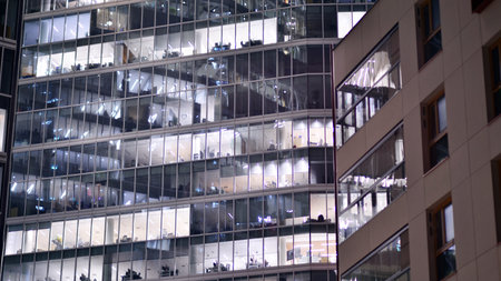 Office building in the evening with lightened workspaces. Modern, glazed skyscraper in financial district. Late hours in the office.の写真素材