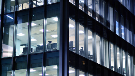 Office building in the evening with lightened workspaces. Modern, glazed skyscraper in financial district. Late hours in the office.の写真素材