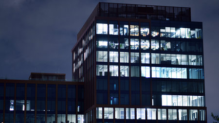 Office building in the evening with lightened workspaces. Modern, glazed skyscraper in financial district. Late hours in the office.の写真素材