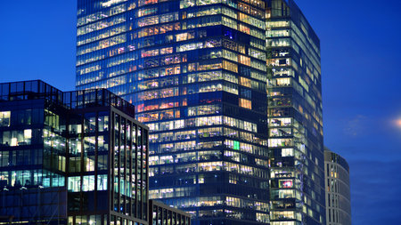 Office building in the evening with lightened workspaces. Modern, glazed skyscraper in financial district. Late hours in the office.の写真素材