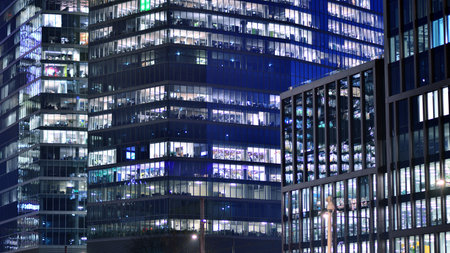 Office building in the evening with lightened workspaces. Modern, glazed skyscraper in financial district. Late hours in the office.の写真素材