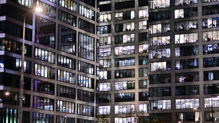 Office building in the evening with lightened workspaces. Modern, glazed skyscraper in financial district. Late hours in the office.の写真素材