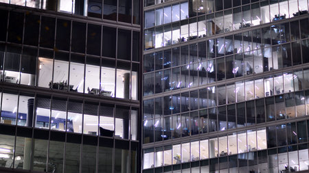 Office building in the evening with lightened workspaces. Modern, glazed skyscraper in financial district. Late hours in the office.の写真素材