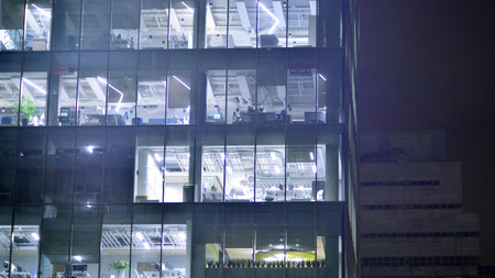 Office building in the evening with lightened workspaces. Modern, glazed skyscraper in financial district. Late hours in the office.の写真素材