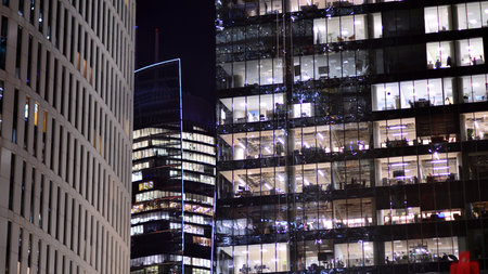 Office building in the evening with lightened workspaces. Modern, glazed skyscraper in financial district. Late hours in the office.の写真素材