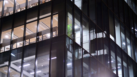 Office building in the evening with lightened workspaces. Modern, glazed skyscraper in financial district. Late hours in the office.の写真素材