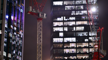 Office building in the evening with lightened workspaces. Modern, glazed skyscraper in financial district. Late hours in the office.の写真素材