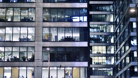 Office building in the evening with lightened workspaces. Modern, glazed skyscraper in financial district. Late hours in the office.の写真素材