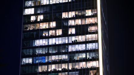 Office building in the evening with lightened workspaces. Modern, glazed skyscraper in financial district. Late hours in the office.の写真素材
