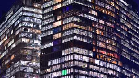 Office building in the evening with lightened workspaces. Modern, glazed skyscraper in financial district. Late hours in the office.の写真素材