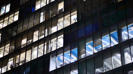 Office building in the evening with lightened workspaces. Modern, glazed skyscraper in financial district. Late hours in the office.の写真素材