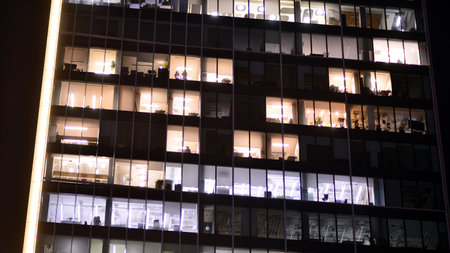 Office building in the evening with lightened workspaces. Modern, glazed skyscraper in financial district. Late hours in the office.の写真素材