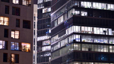 Office building in the evening with lightened workspaces. Modern, glazed skyscraper in financial district. Late hours in the office.の写真素材