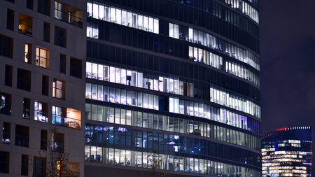 Office building in the evening with lightened workspaces. Modern, glazed skyscraper in financial district. Late hours in the office.の写真素材