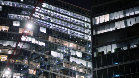 Office building in the evening with lightened workspaces. Modern, glazed skyscraper in financial district. Late hours in the office.の写真素材