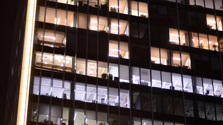 Office building in the evening with lightened workspaces. Modern, glazed skyscraper in financial district. Late hours in the office.の写真素材