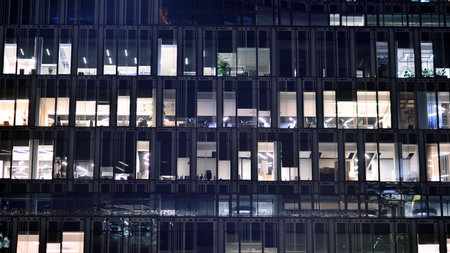 Office building in the evening with lightened workspaces. Modern, glazed skyscraper in financial district. Late hours in the office.の写真素材