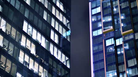 Office building in the evening with lightened workspaces. Modern, glazed skyscraper in financial district. Late hours in the office.の写真素材