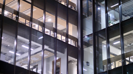 Office building in the evening with lightened workspaces. Modern, glazed skyscraper in financial district. Late hours in the office.の写真素材