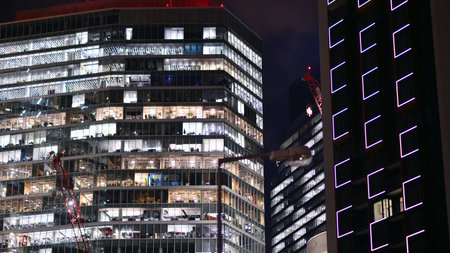 Office building in the evening with lightened workspaces. Modern, glazed skyscraper in financial district. Late hours in the office.の写真素材