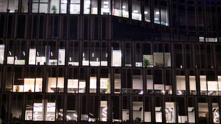 Office building in the evening with lightened workspaces. Modern, glazed skyscraper in financial district. Late hours in the office.の写真素材